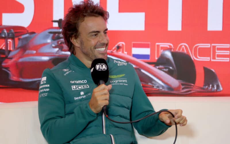 Fernando Alonso in a green jacket holding a microphone at the v2023 Dutch Grand Prix
