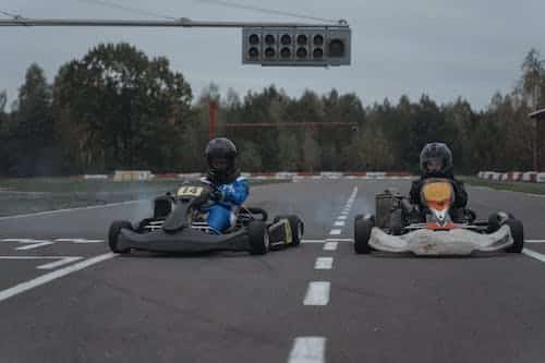 two people riding go kart cars on a road