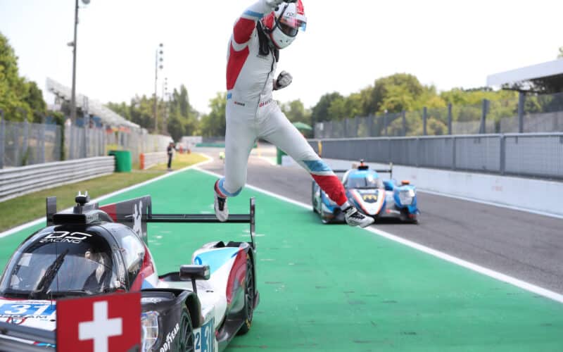 a man in a red and white suit is jumping over a race car