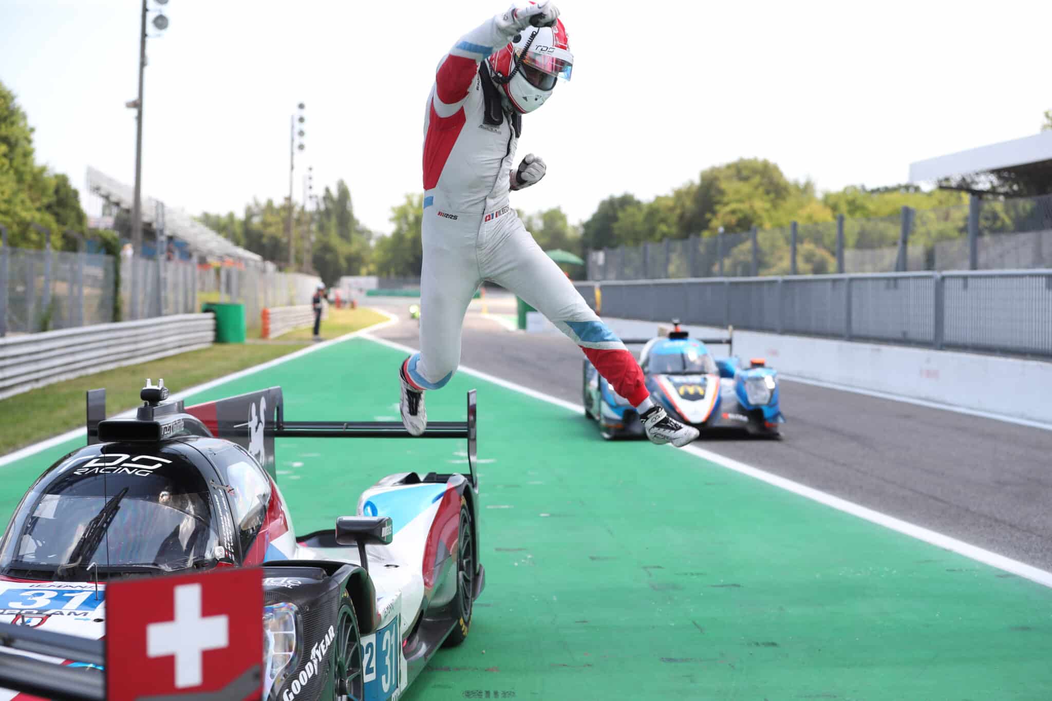 a man in a red and white suit is jumping over a race car