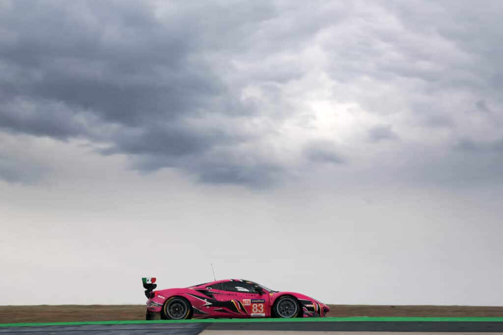 a pink sports car driving on a track under a cloudy sky