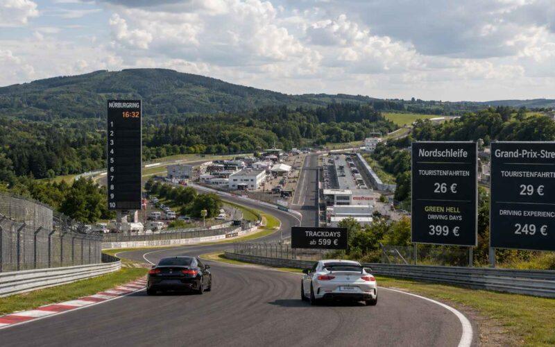 Deux Porsche sur circuit asphalté, encadrées par de grands panneaux noirs affichant les tarifs de la Nordschleife et du GP.